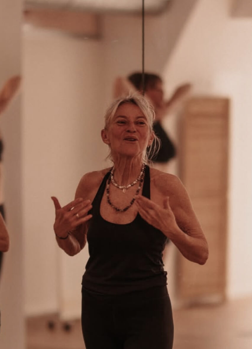 Smiling elderly woman in a black tank top speaking passionately during a movement or wellness class—authentic lifestyle and community content in Ibiza by vIBZ Marketing.
