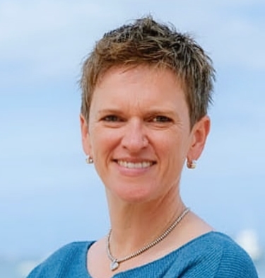Portrait of a woman with short hair and a blue top, smiling against the sky. Part of the vIBZ Marketing team.