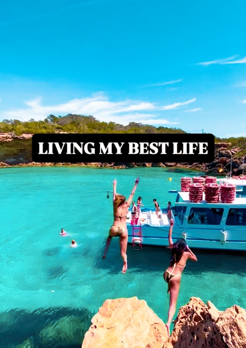 People jumping into turquoise water from rocks near a boat in Ibiza—adventurous lifestyle and travel content by vIBZ Marketing.