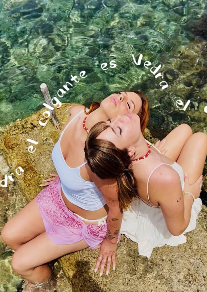 Two women sitting by the sea in Ibiza, leaning back with closed eyes under the sun—natural lifestyle and fashion content creation by vIBZ Marketing.