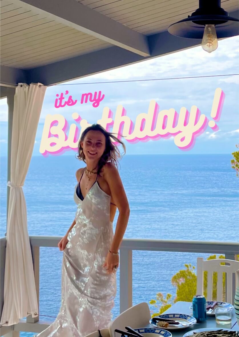 Smiling woman in white dress celebrating birthday on terrace with sea view in Ibiza—private event and lifestyle content by vIBZ Marketing.
